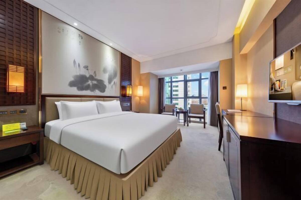 A hotel room with a large bed, bedside tables, a desk, and a view of the outside.