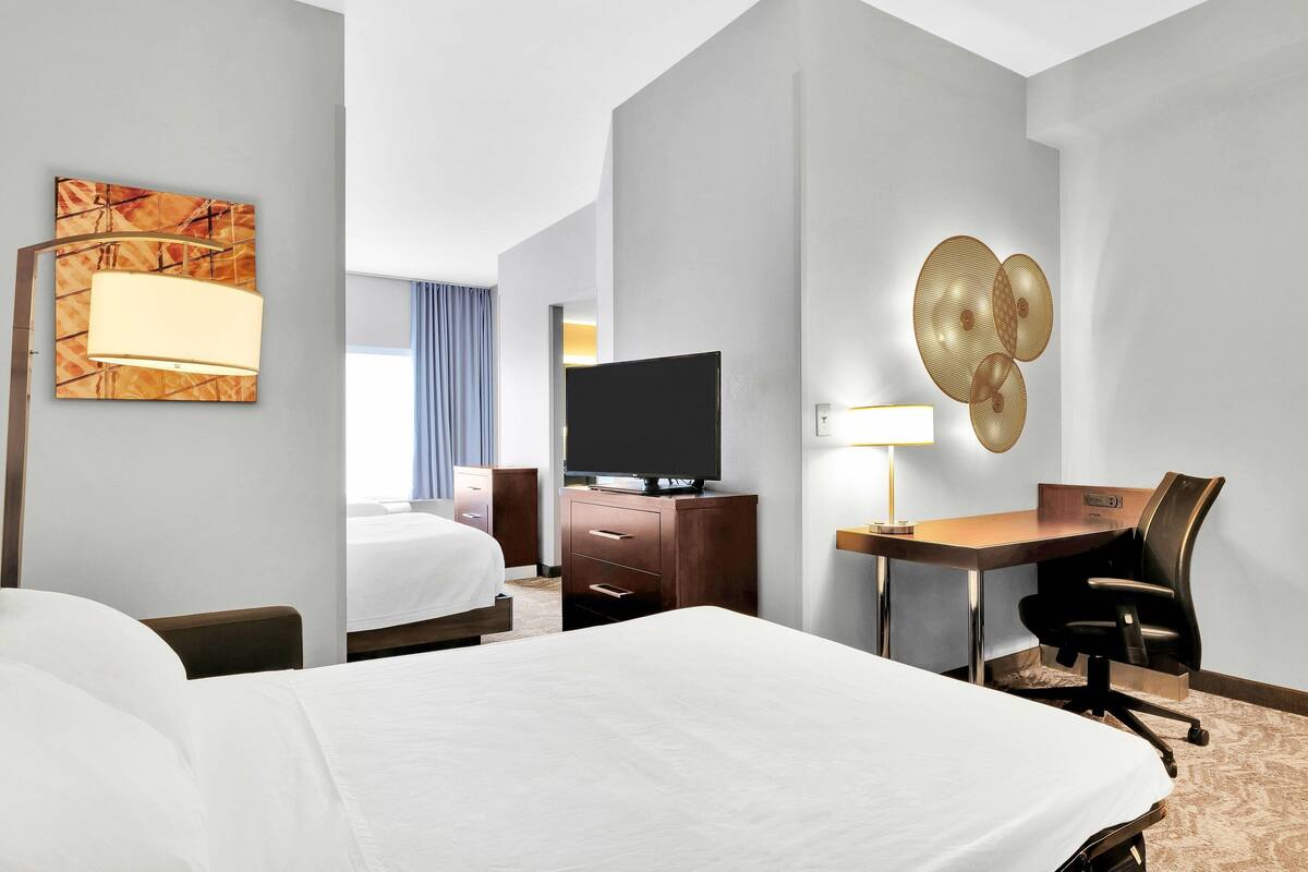 Una habitación de hotel con una cama grande, un escritorio con silla, un televisor y una lámpara de pared.