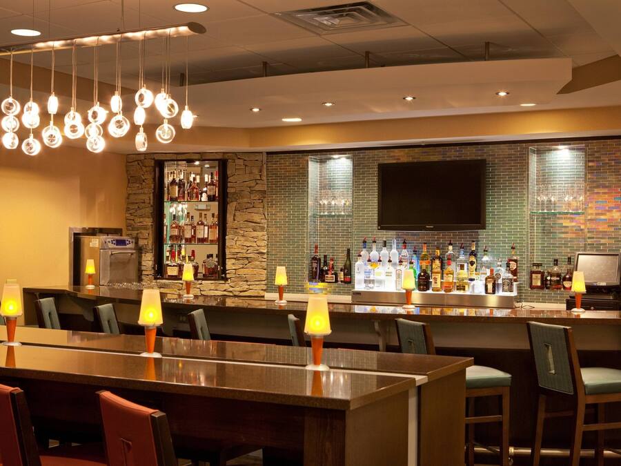 A bar area with a long counter, multiple chairs, and a television mounted on the wall.