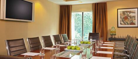 A conference room with a large table, chairs, a flat-screen TV, and a window with curtains.