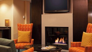 Una sala de estar moderna con dos sillones naranja estampados, una mesa de centro de cristal, un televisor de pantalla plana sobre la chimenea y una revista sobre la mesa.