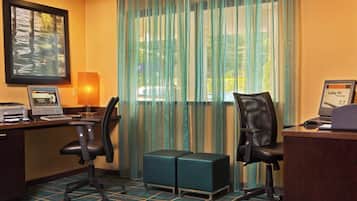 Habitación de hotel con escritorio, dos sillas de oficina, una computadora portátil, una impresora y un pequeño taburete verde.