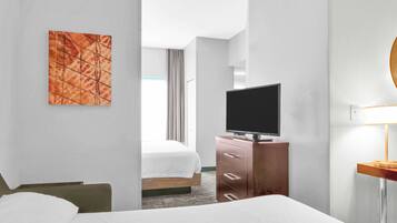 Une chambre d’hôtel avec un lit, un téléviseur posé sur une commode en bois, un tableau au mur et une lampe sur une table de chevet.