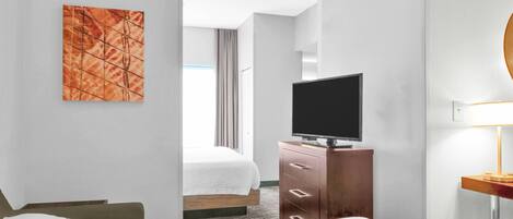 Una habitación de hotel con una cama, un televisor sobre un aparador de madera, un cuadro en la pared y una lámpara sobre una mesita.