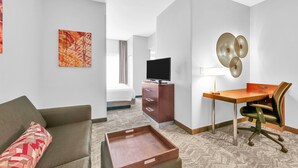 Habitación de hotel con cama, escritorio con silla, televisión y obras de arte en las paredes.