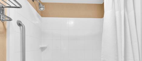 A bathroom with white tiles, a shower with a handheld showerhead, a grab bar, and a white towel.