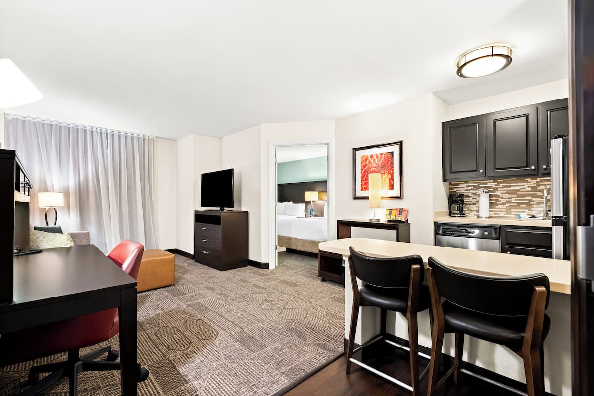 A hotel room with a dining area, kitchenette, and a bed.