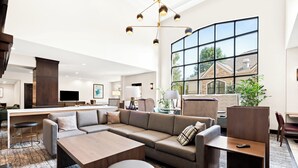 A modern living room with a sectional sofa, a wooden coffee table, and a large window offering a view of the outside. - Staybridge Suites Cincinnati North by IHG (West Chester)