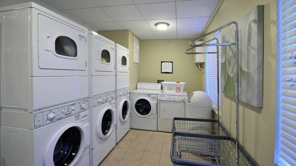 A laundry room with stacked washers and dryers, a basket, and a wall-mounted drying rack.