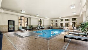 A spacious indoor swimming pool with clear blue water, surrounded by lounge chairs and a few tables. - Staybridge Suites Cincinnati North by IHG (West Chester)