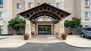A building entrance with a stone facade, a covered entrance, and two potted plants with red flowers. - Staybridge Suites Cincinnati North by IHG (West Chester)