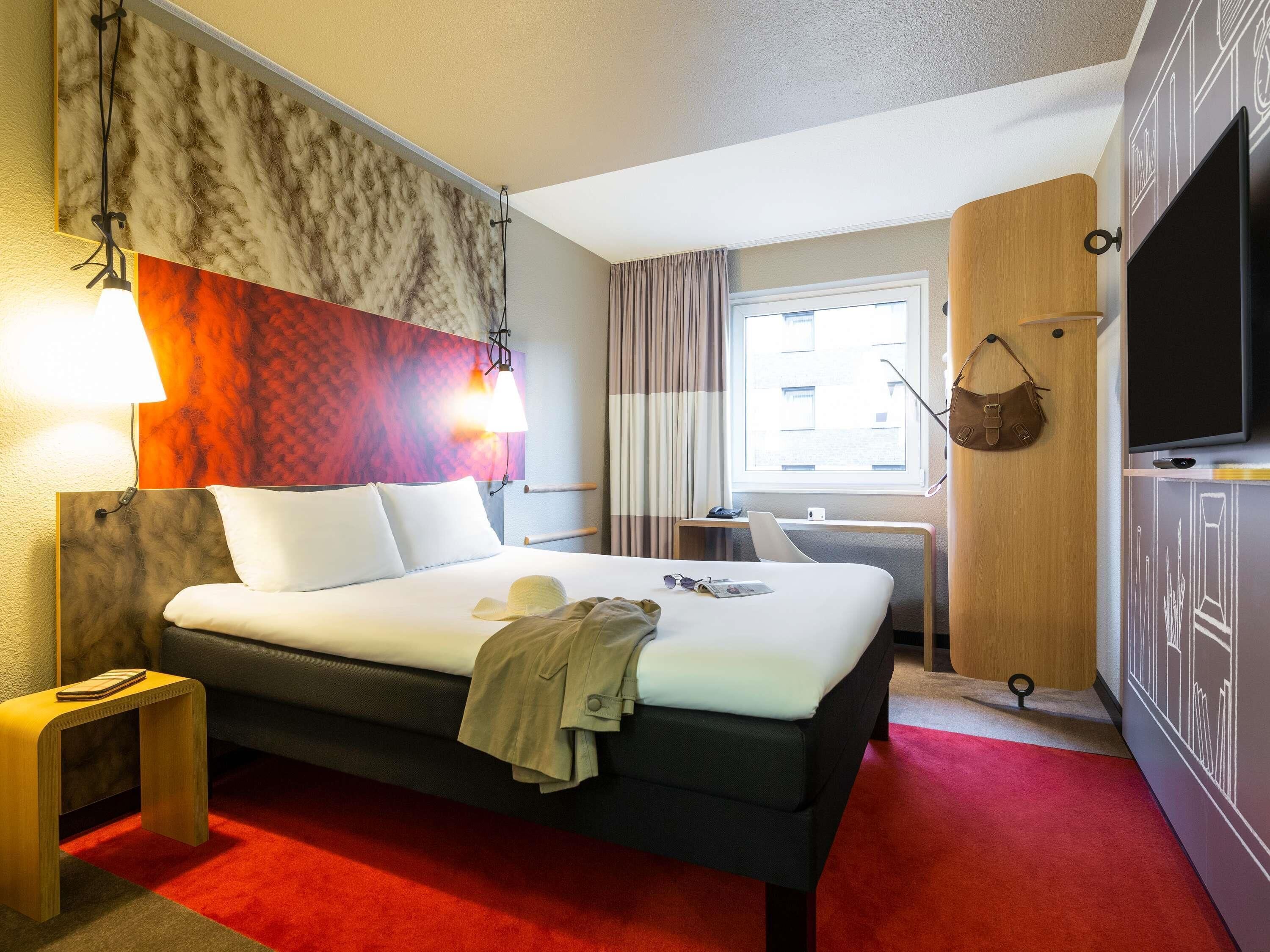 Une chambre d’hôtel avec un lit, des lampes de chevet, un bureau, une télévision et une fenêtre avec des rideaux.