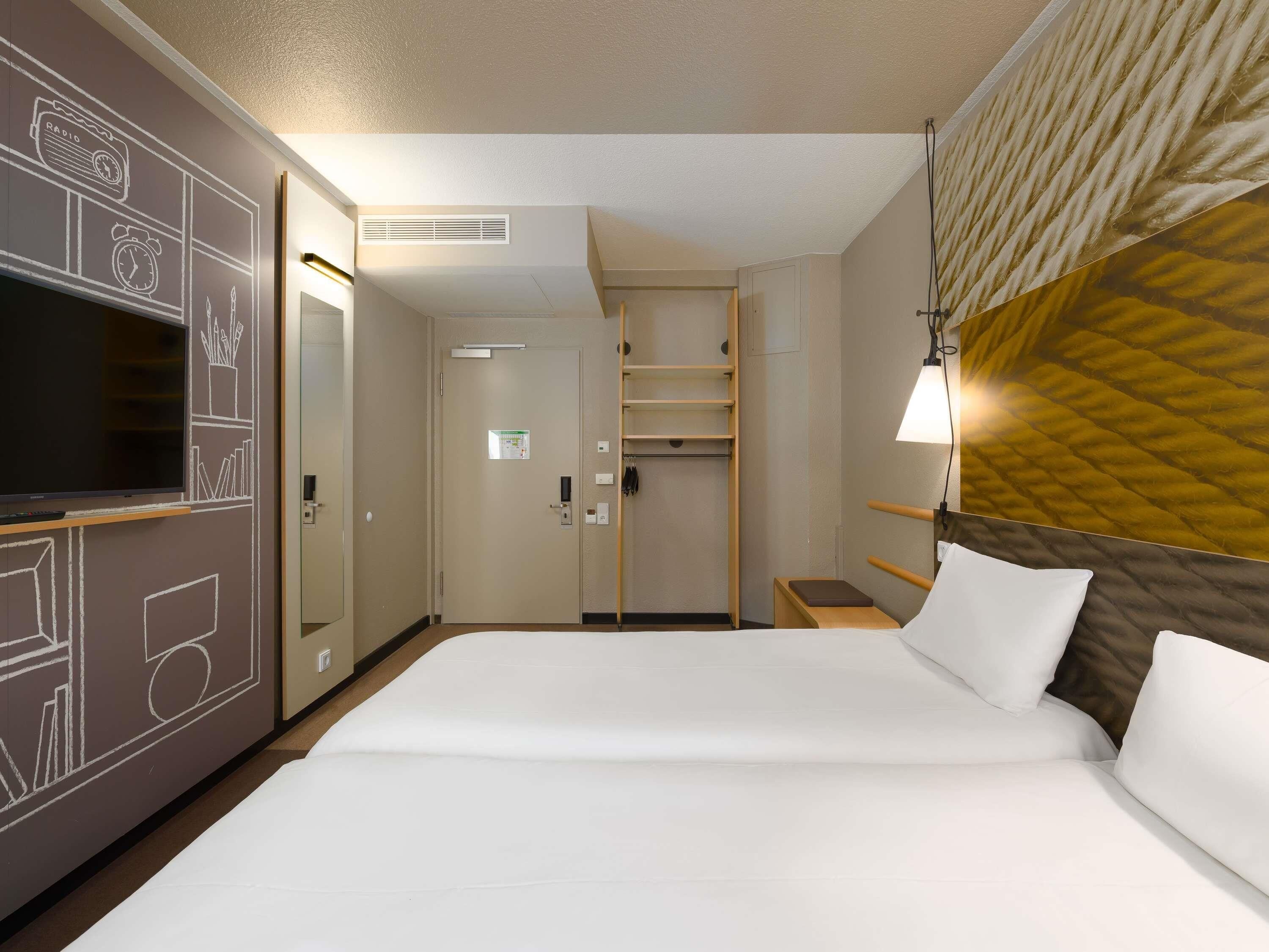 Une chambre d’hôtel équipée d’un lit, d’une télévision, d’une armoire, d’une table de chevet et d’une lampe.