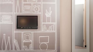 Un mur sur lequel est fixé un téléviseur à écran plat, au-dessus d’une œuvre d’art murale de style tableau noir représentant divers objets, comme des livres, une radio et une horloge.