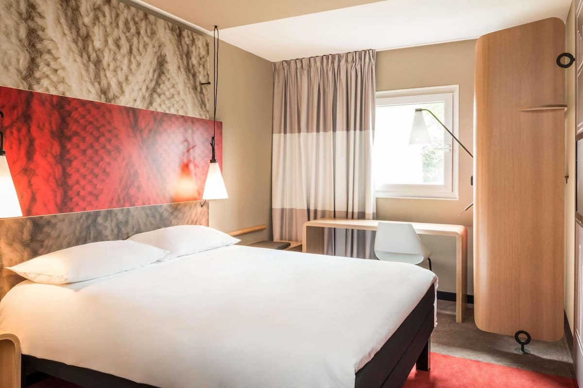A hotel room with a bed, desk, and wardrobe.