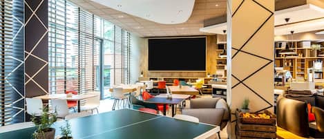 Ein moderner Konferenzraum mit einem großen Tisch, Stühlen, einer Projektionsleinwand und einem Bücherregal.