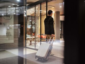 Un homme, une valise à la main, se trouve dans un hall d’entrée moderne aux murs de verre, avec un espace détente et une enseigne bien visible.