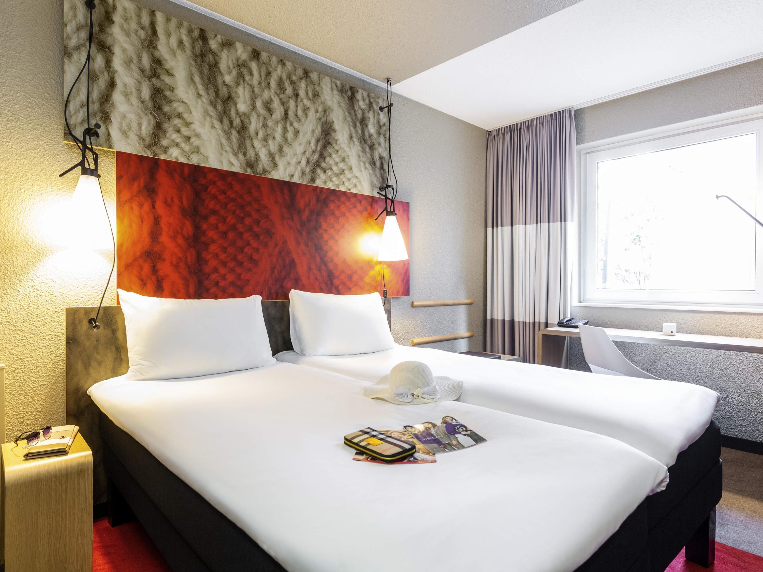 Une chambre d’hôtel avec un grand lit, deux lampes de chevet, un bureau avec une chaise et une fenêtre avec des rideaux.