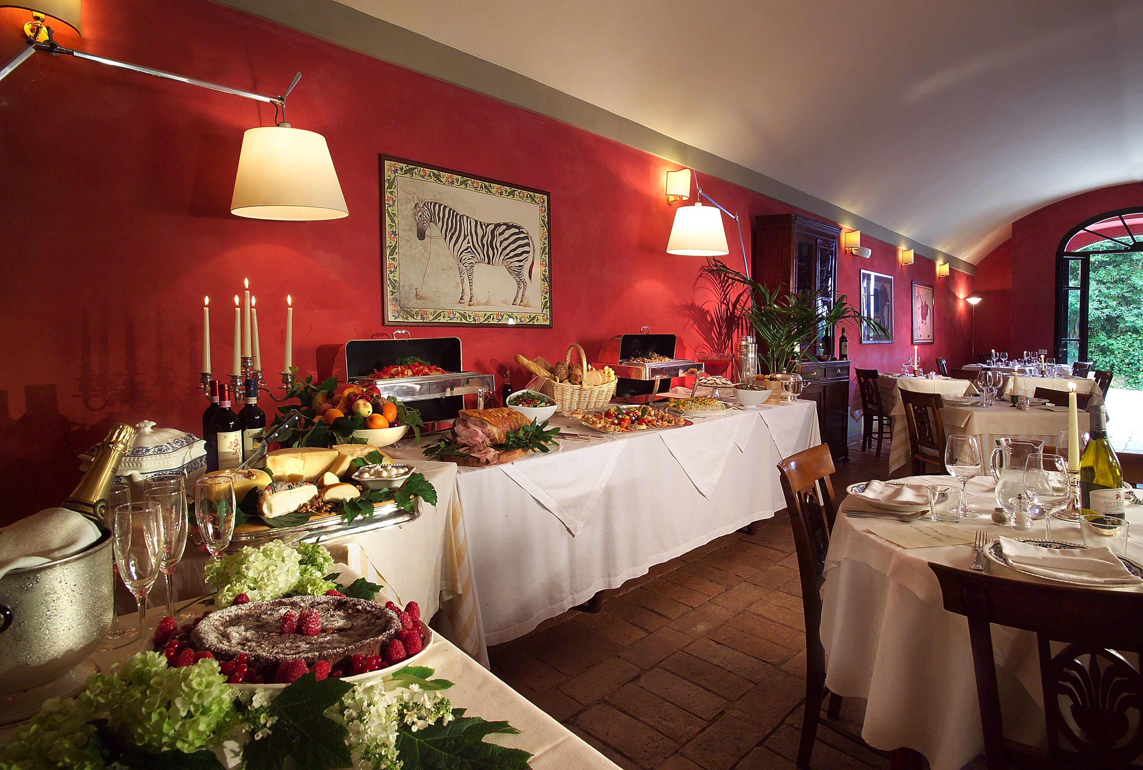 Un coin repas avec des tables dressées pour le repas, un tableau représentant une zèbre accroché au mur et un mur rouge.