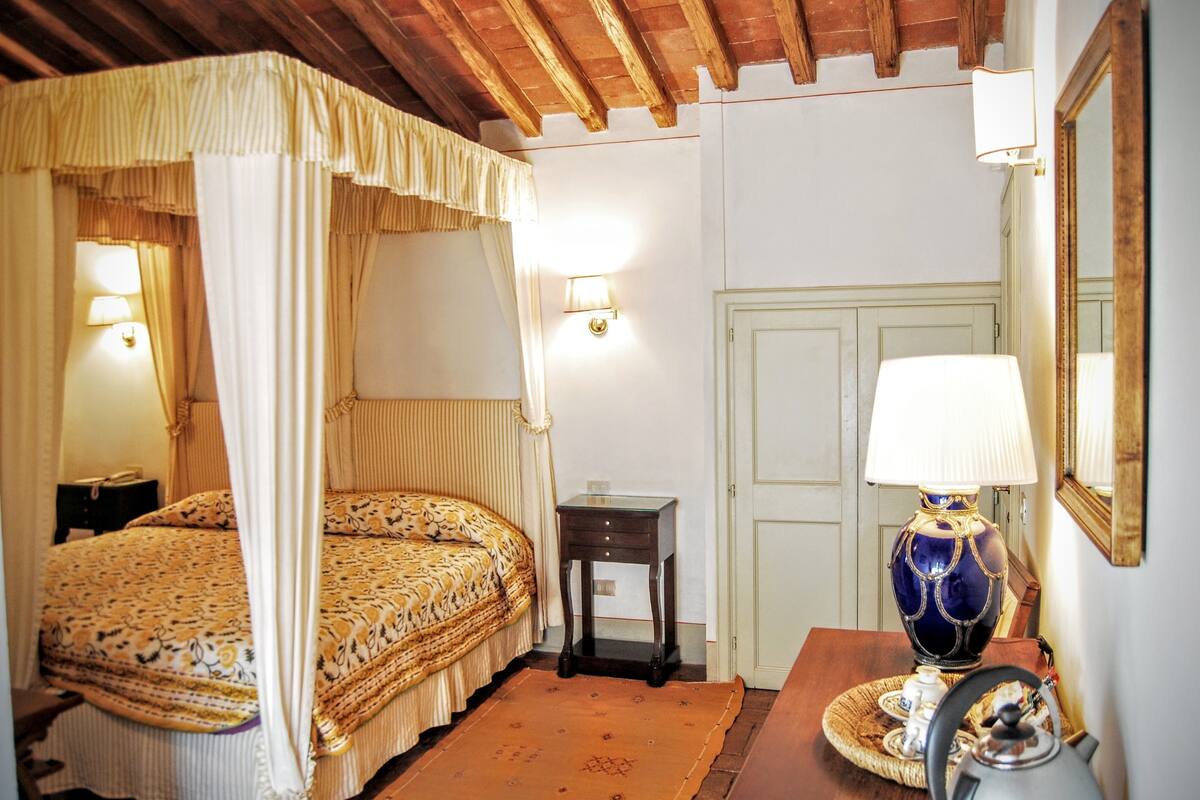 A bedroom with a four-poster bed, bedside lamps, a small table with a lamp, and a mirror on the wall.