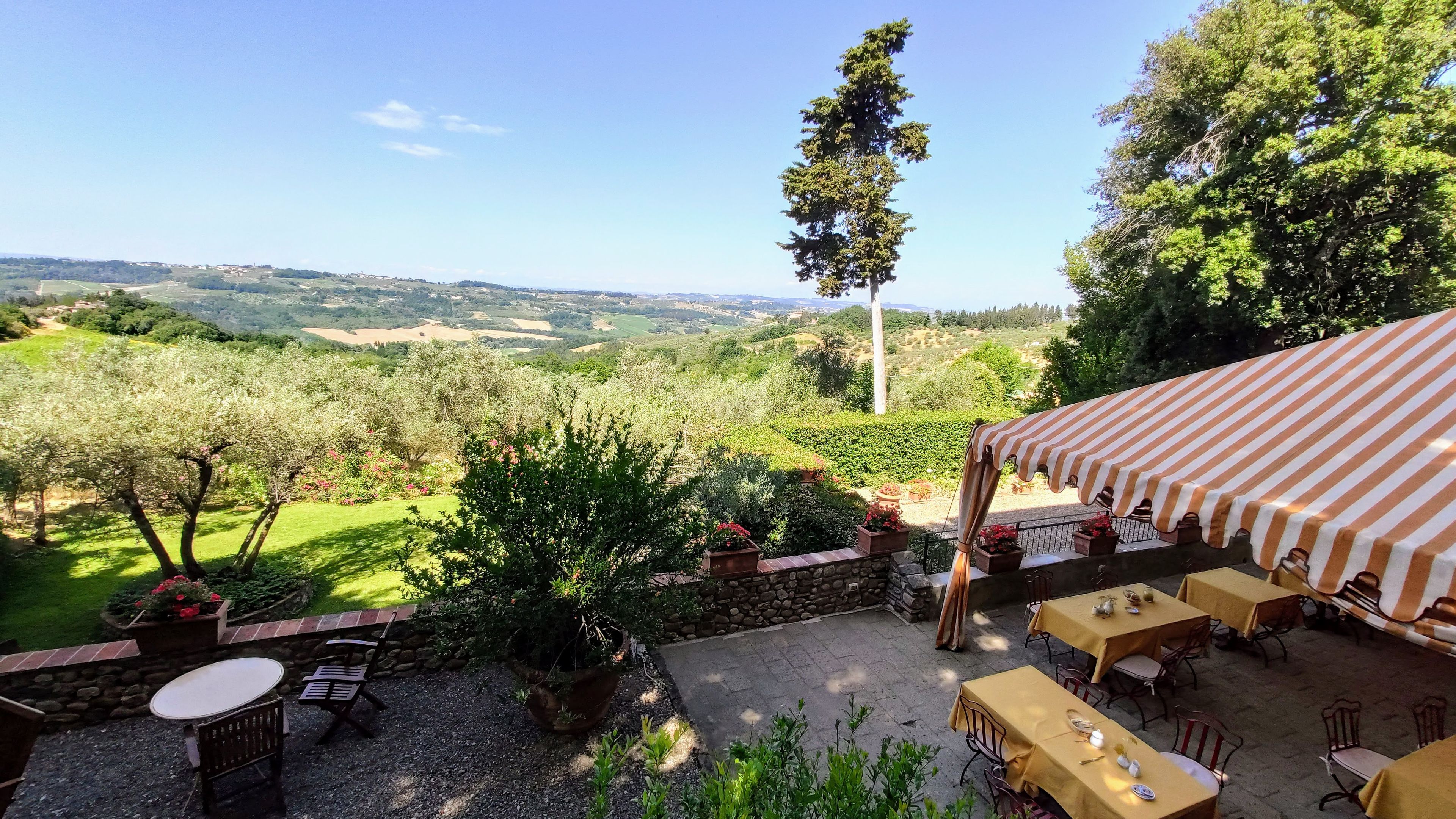 Eine Terrasse im Freien mit Tischen und Stühlen, mit Blick auf ein malerisches Tal.