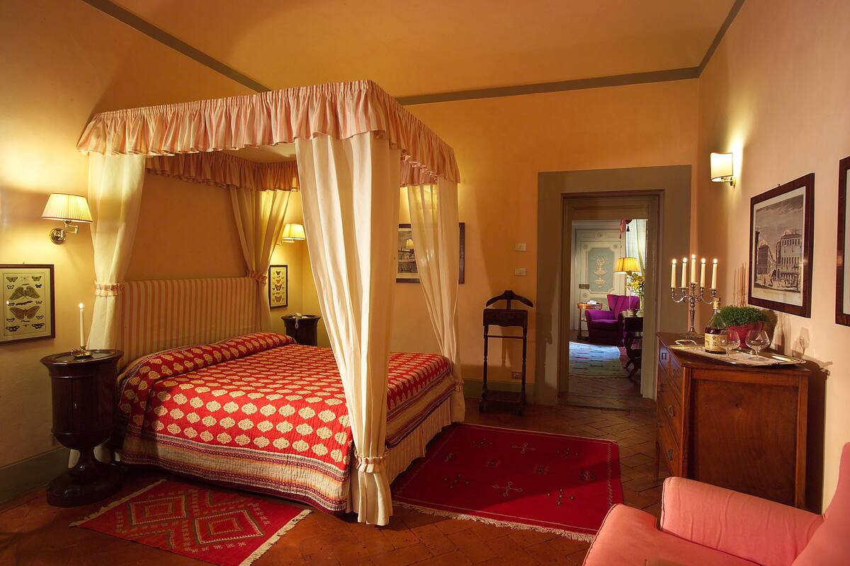 A bedroom with a four-poster bed, a wooden dresser, and a red rug.