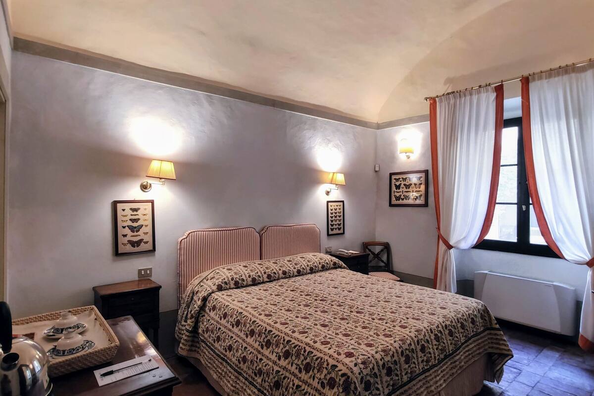 A bedroom with a bed, bedside tables, a lamp, a window with curtains, and wall art.