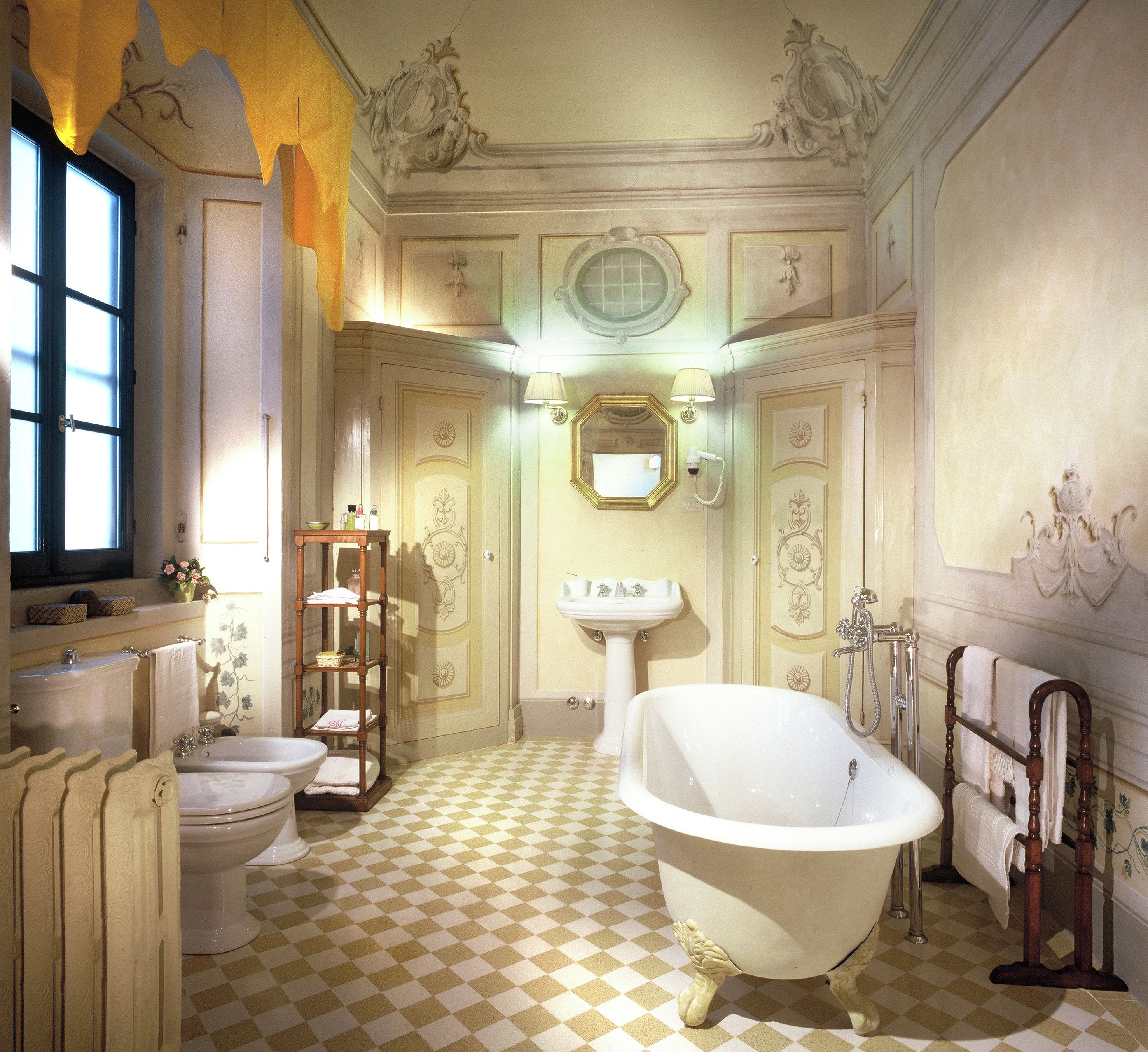 A bathroom with a checkered floor, a freestanding bathtub, a pedestal sink, and a toilet.