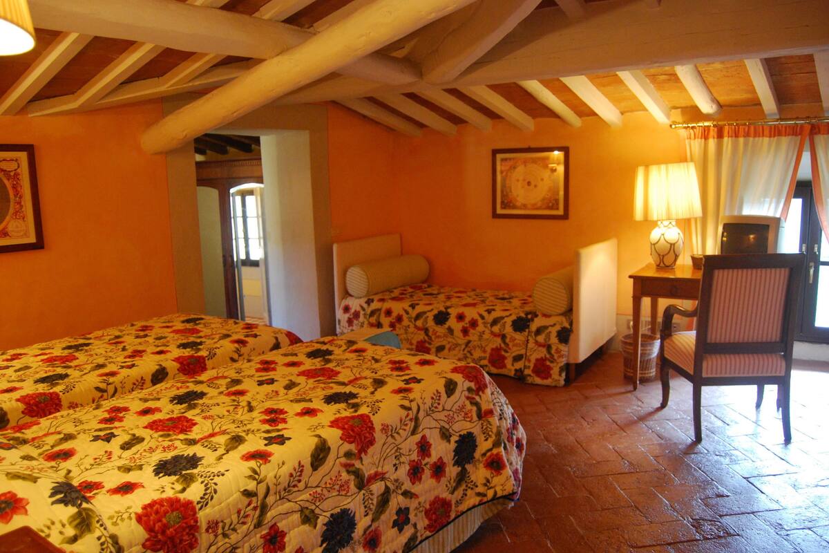 A room with two beds, a desk, and a chair. There is a door leading to another room.