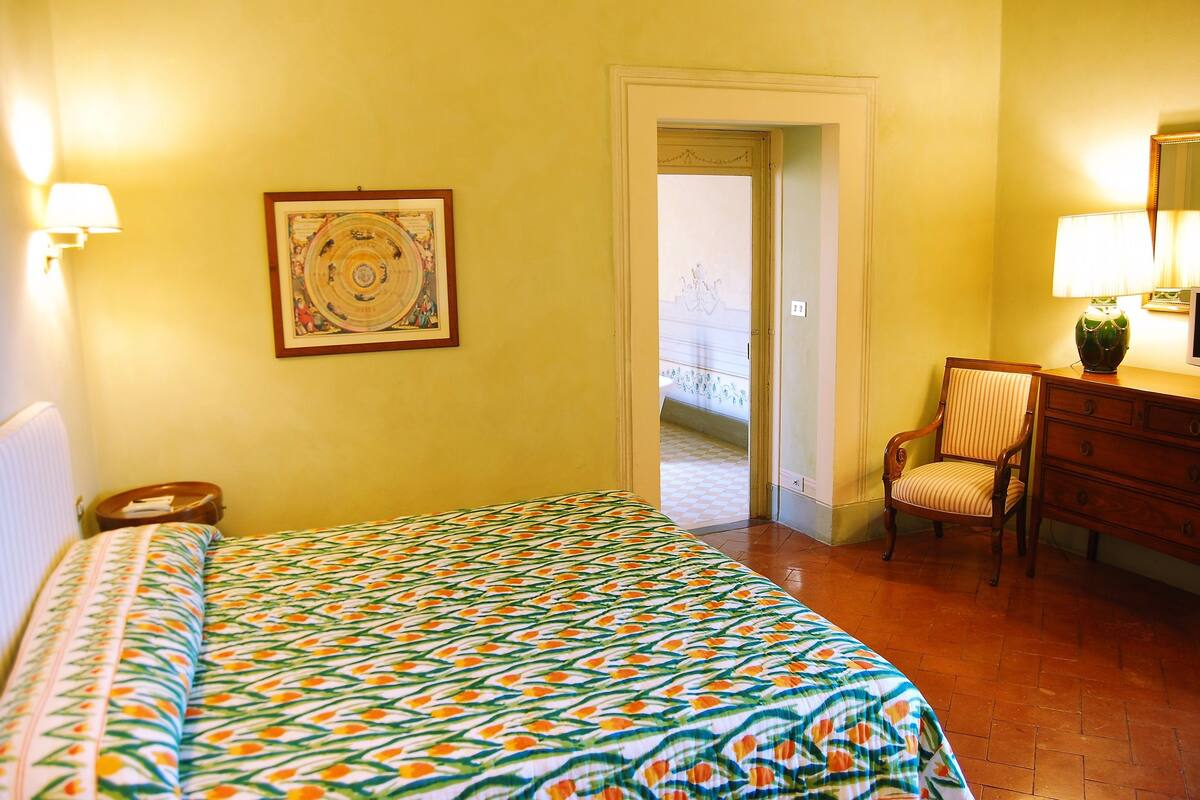 A hotel room with a bed, a chair, a dresser, and a door leading to a balcony.