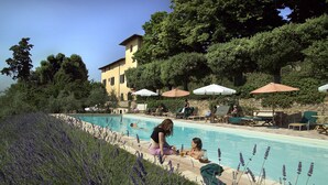 Zona junto a la piscina con piscina, sillones de descanso y un edificio al fondo.