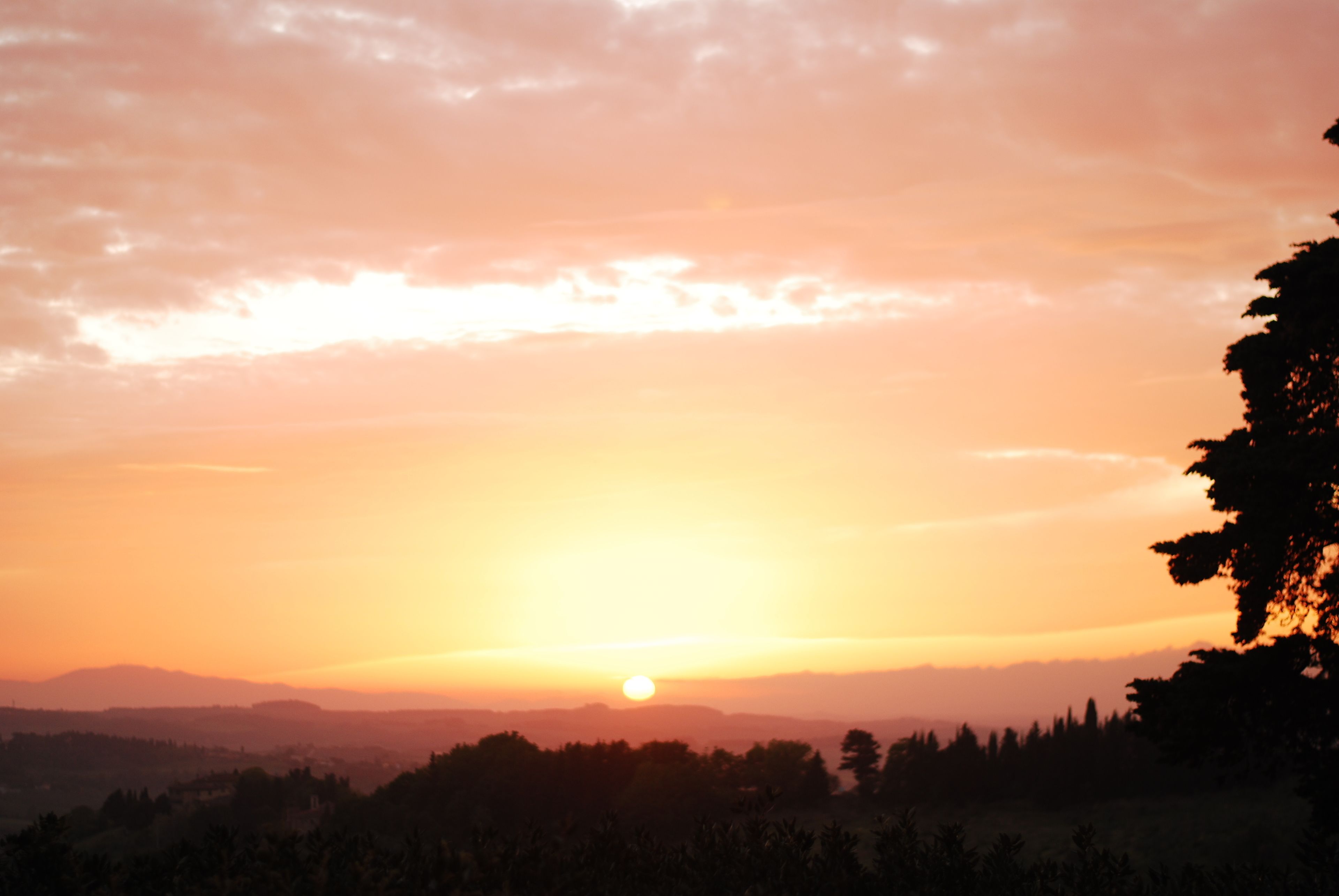 A sunset over a mountainous landscape with silhouettes of trees and a clear sky.