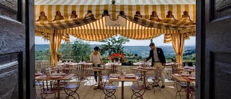 Un área de comedor al aire libre con mesas y sillas, un dosel a rayas y vistas al paisaje.