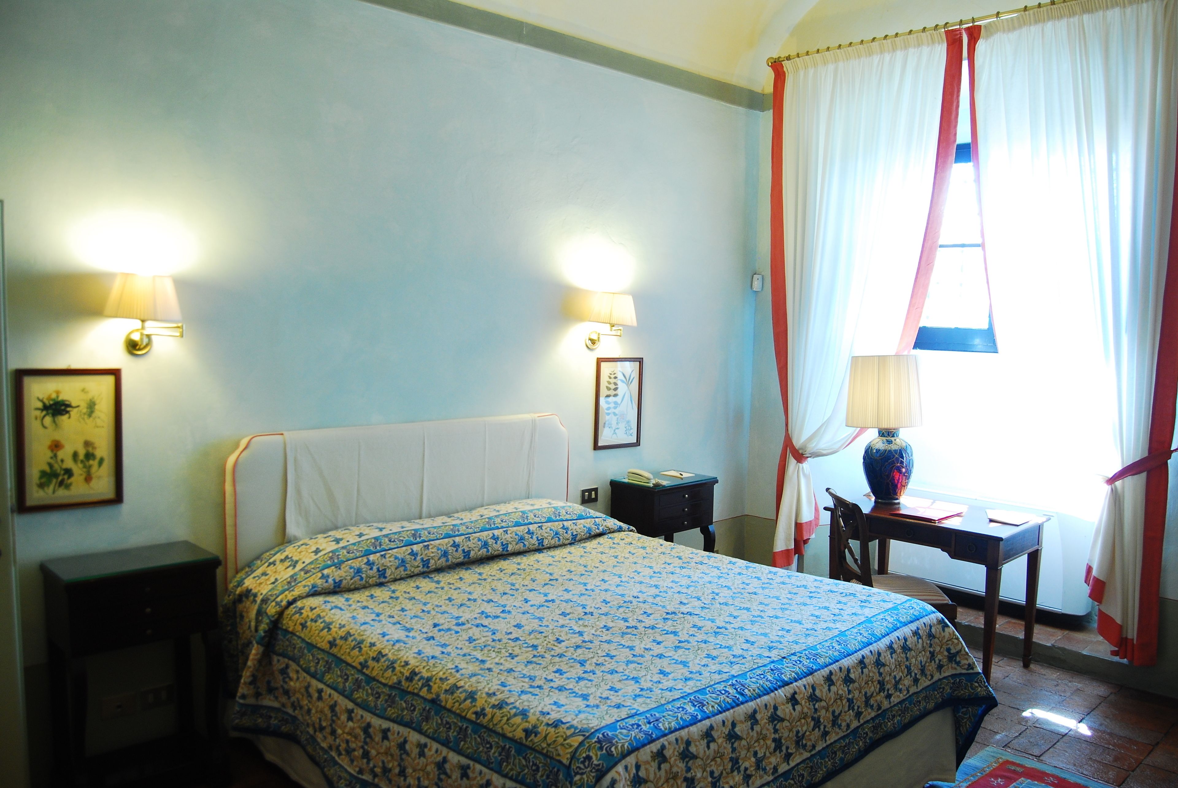 Una camera da letto con un letto, abat-jour, una scrivania e una finestra con tende.