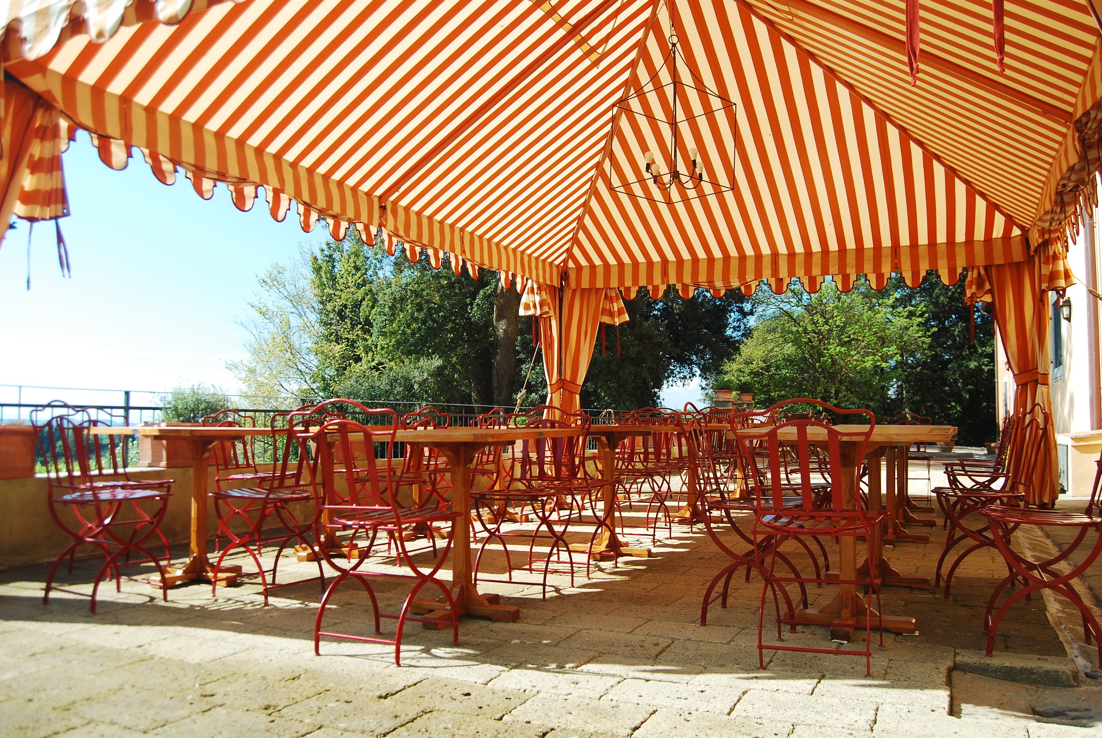Un espace extérieur aménagé avec des parasols à rayures et des chaises en métal rouge.