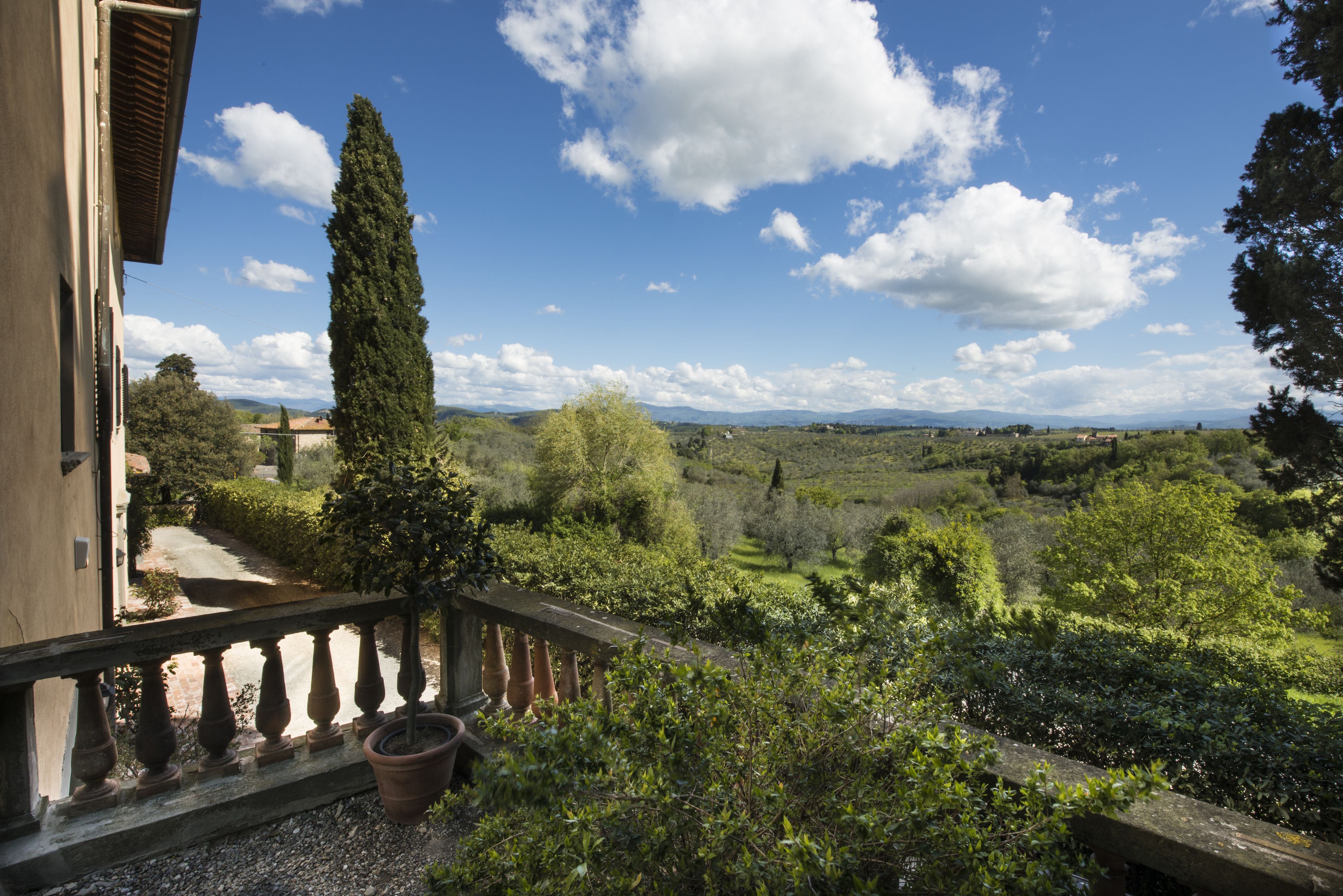 A balcony with a view of a lush landscape, including trees and distant hills.