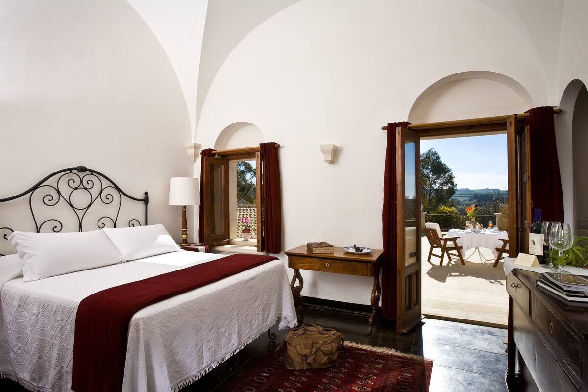 A bedroom with a bed, a desk, and a view of an outdoor patio.