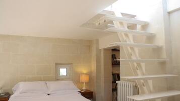 A bedroom with a bed, a nightstand, a lamp, a radiator, and a staircase.
