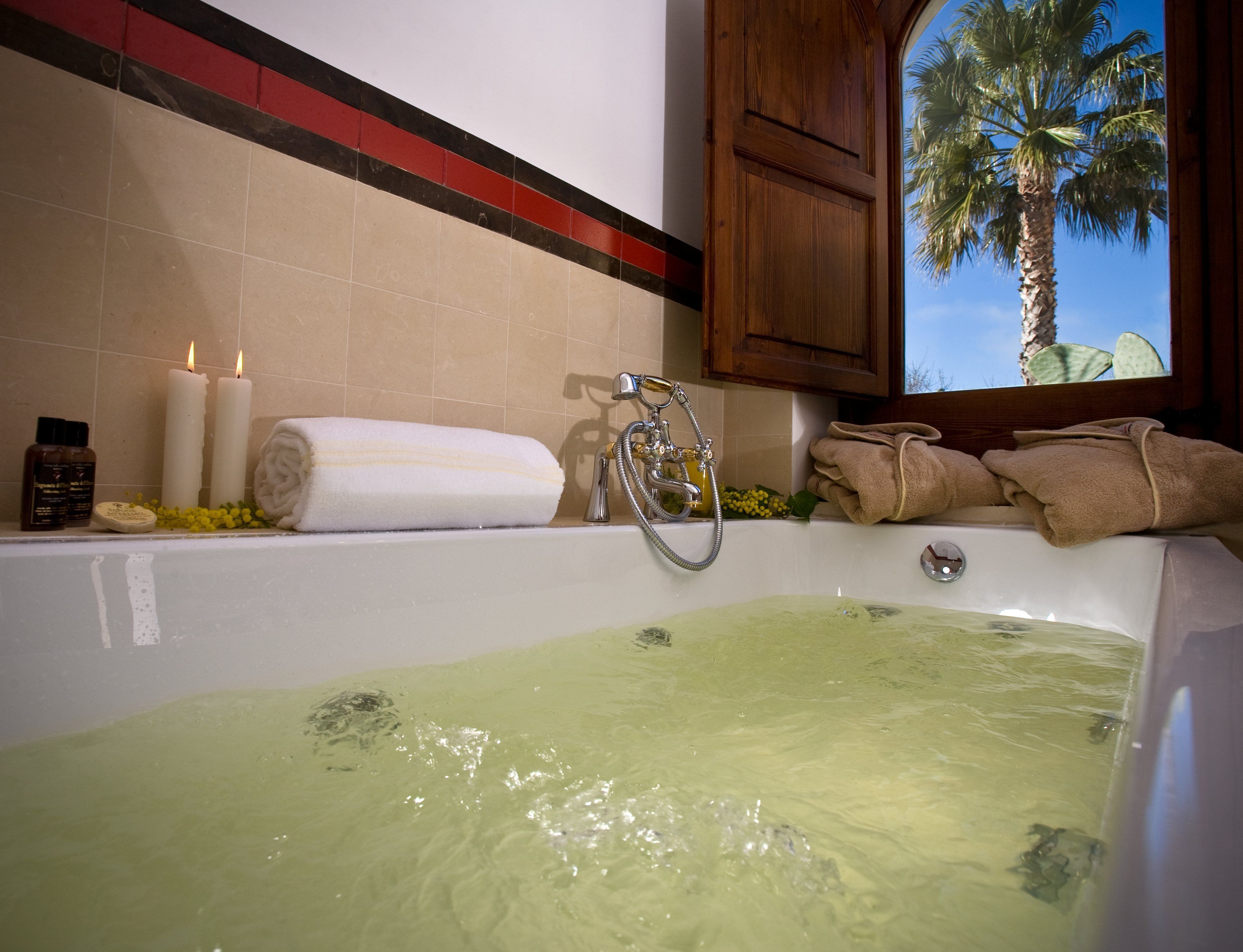 Eine Badewanne mit grünlich gefärbtem Wasser, eine Duschbrause und Handtücher.