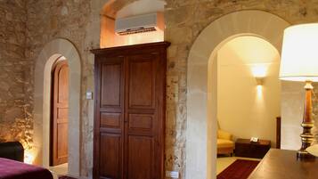 Une pièce aux murs de pierre, avec une armoire en bois, un lit recouvert d’une couverture rouge et une lampe.