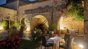 Un área de comedor al aire libre con arcos de piedra, mesas, sillas y plantas en macetas.