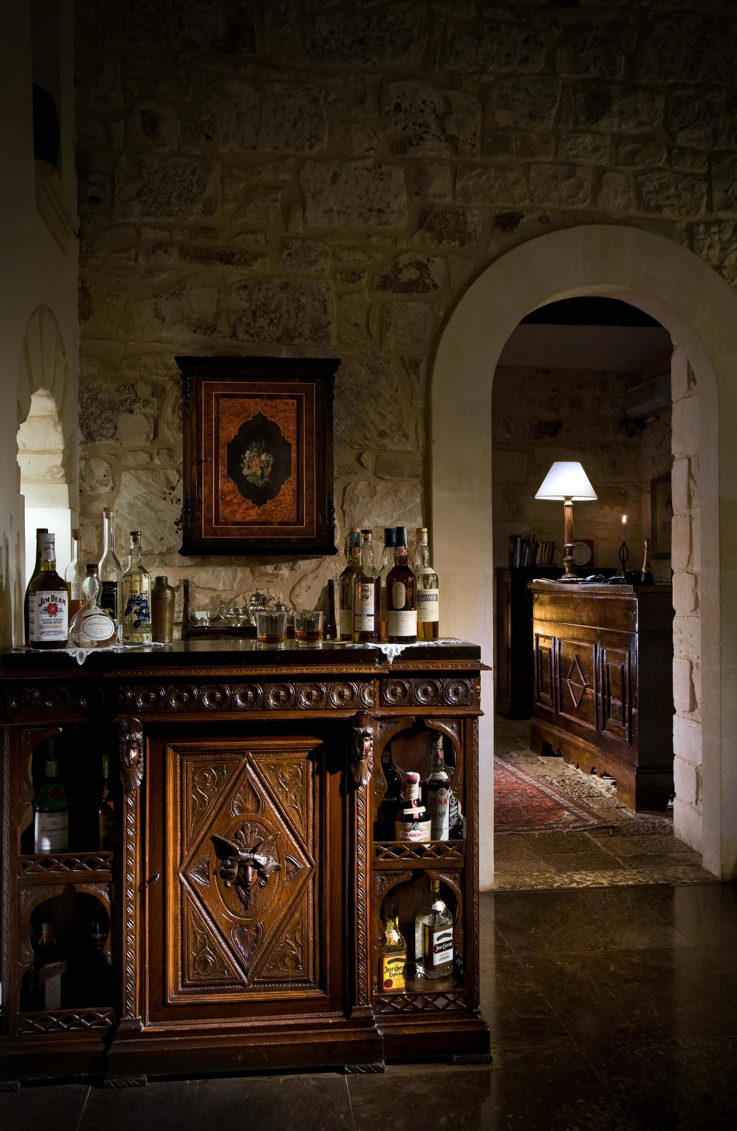 Angolo bar con parete in pietra, mobiletto in legno e diverse bottiglie.