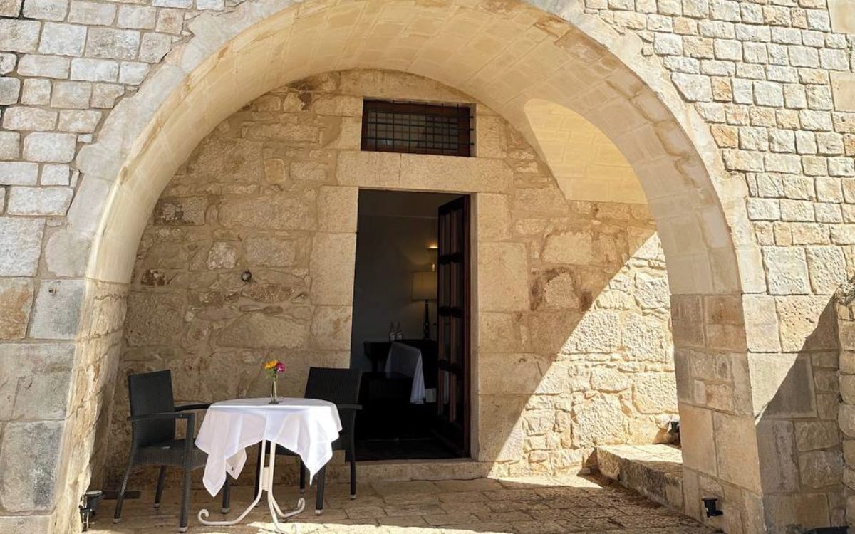 An outdoor seating area with a table and chairs under a stone archway.