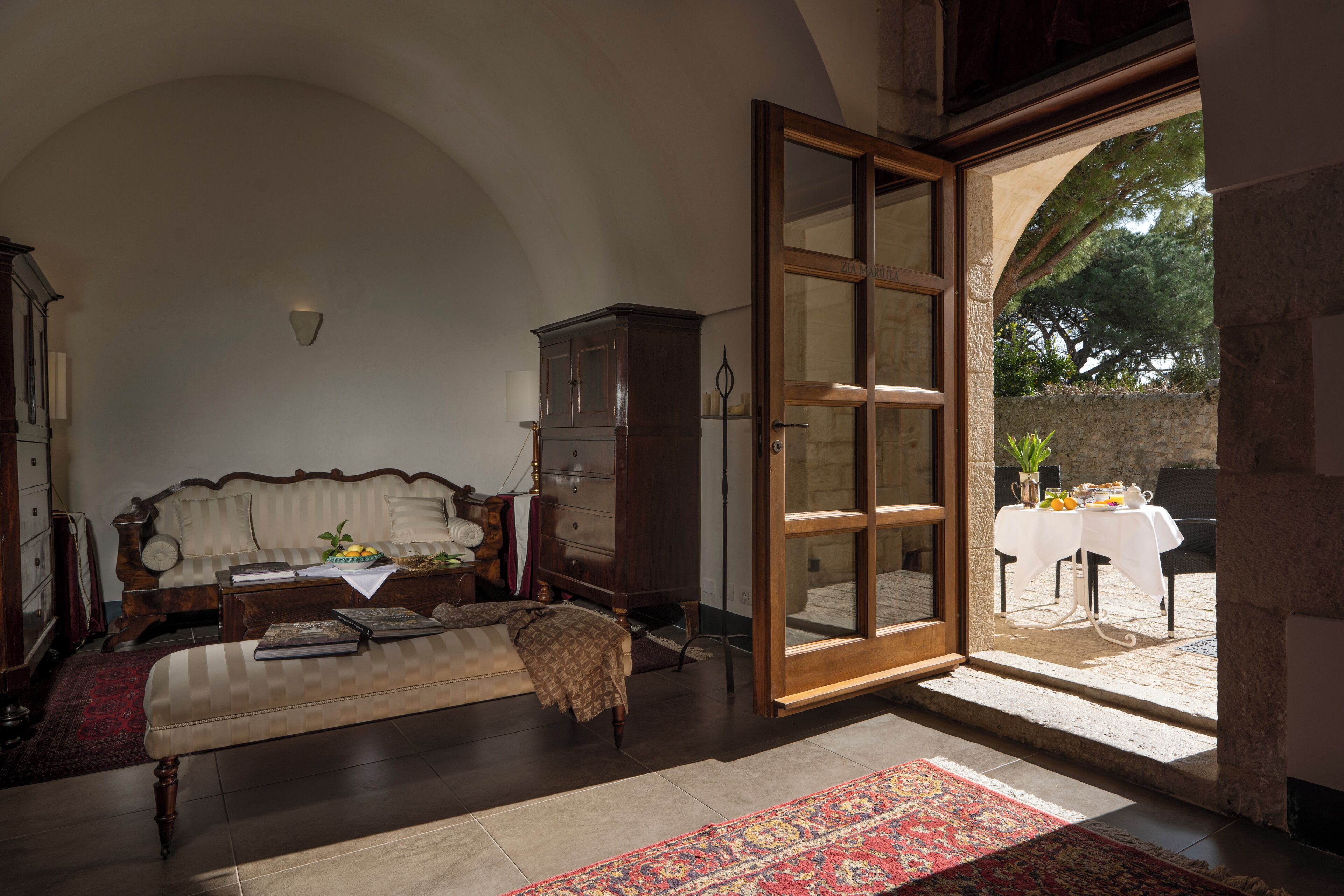 Ein geräumiges Wohnzimmer mit einem großen Fenster, einem Sofa, einem Holzschrank und einem Essbereich, der durch das Fenster sichtbar ist.