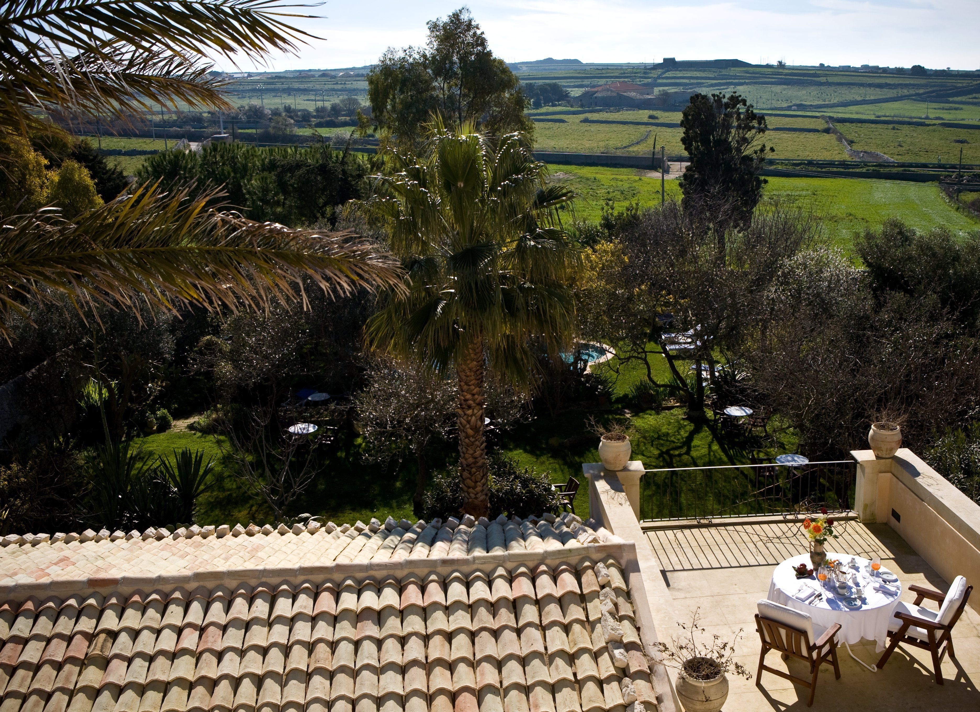 Una terrassa amb teulada a través de la qual es veuen un jardí exuberant i paisatge rural.