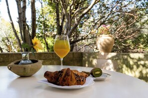 A table with a croissant, a glass of orange juice, a kiwi, and a small vase with a flower. - Hotel Eremo della Giubiliana (Ragusa)