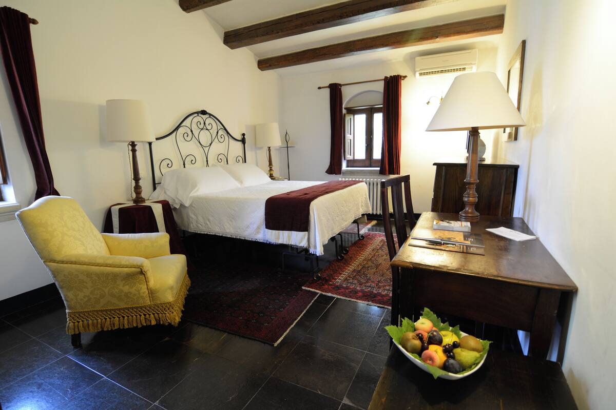 A bedroom with a bed, a chair, a desk, and a fruit bowl.