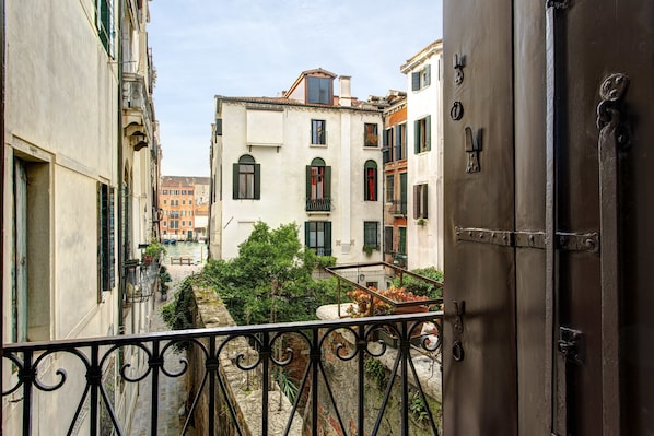A narrow street with buildings on either side, a balcony with a wrought iron railing, and a door with a metal handle.