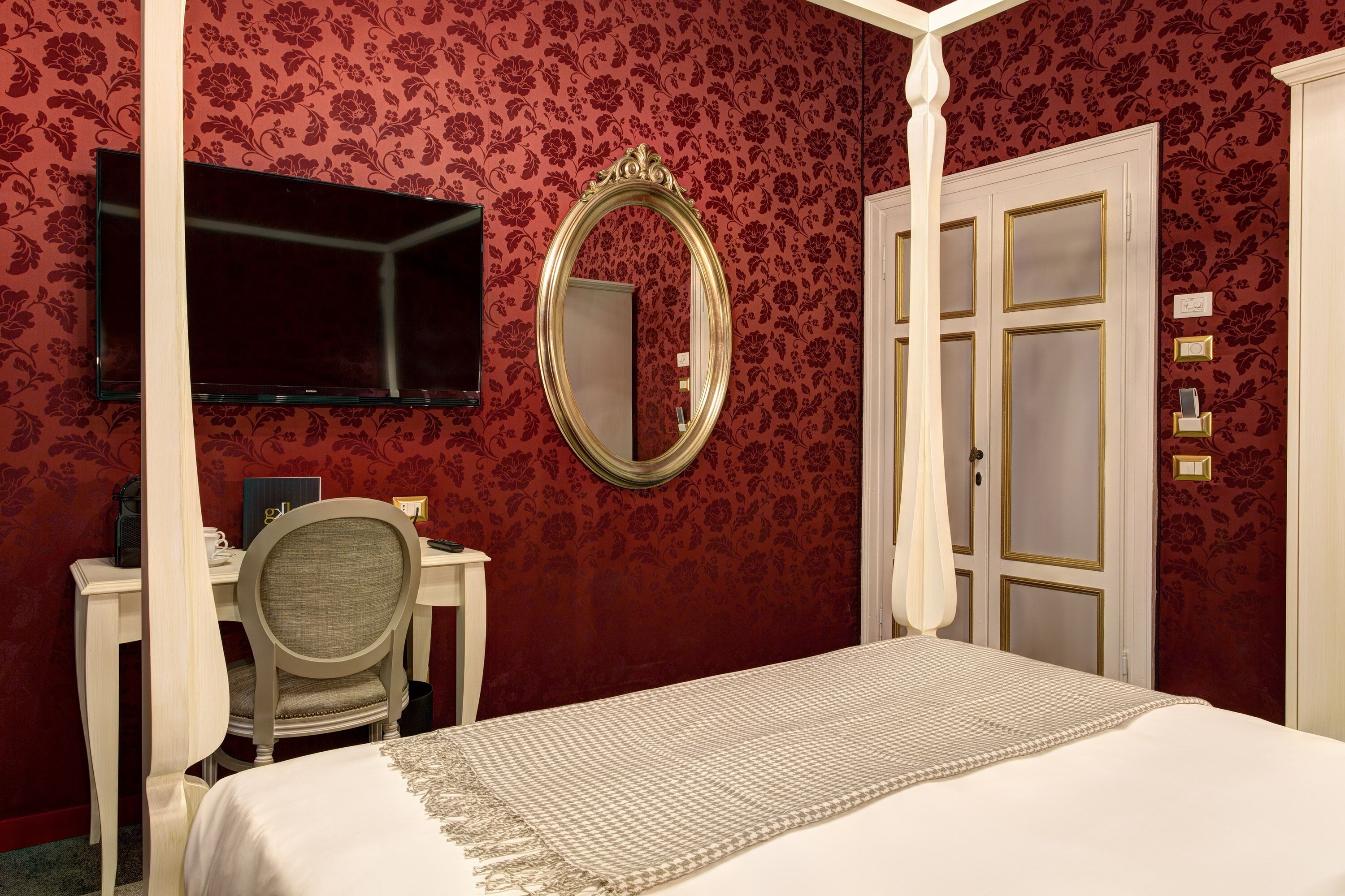 A bedroom with a four-poster bed, a desk with a chair, a television, and a mirror on the wall.