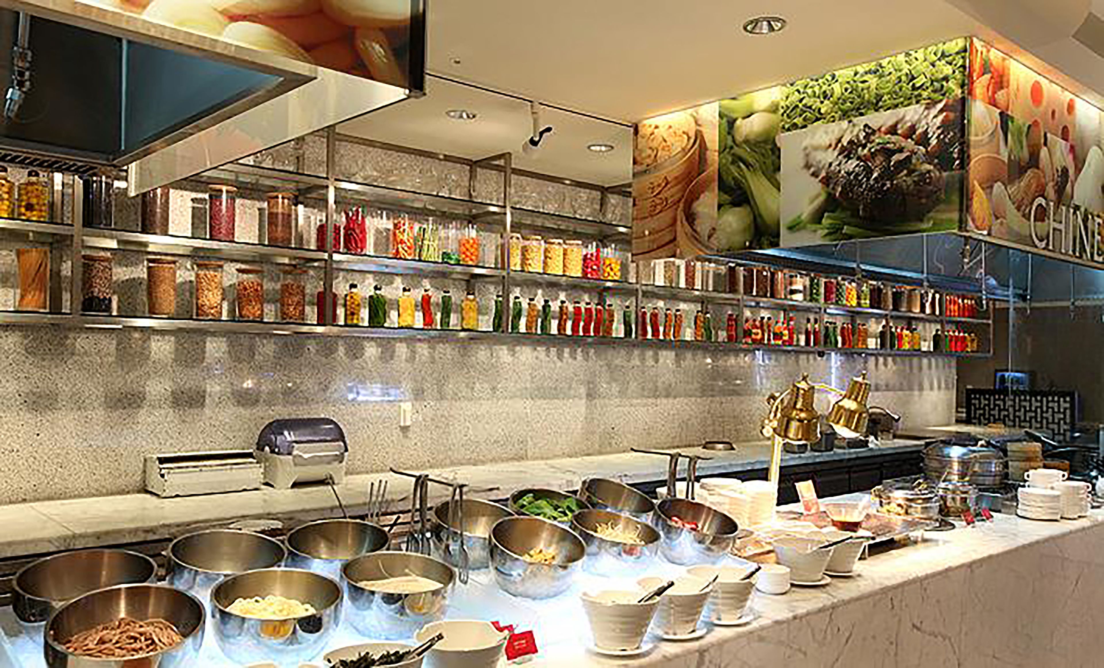 Uma área de buffet com diversas estações de comida, variedade de acompanhamentos e grande seleção de bebidas.